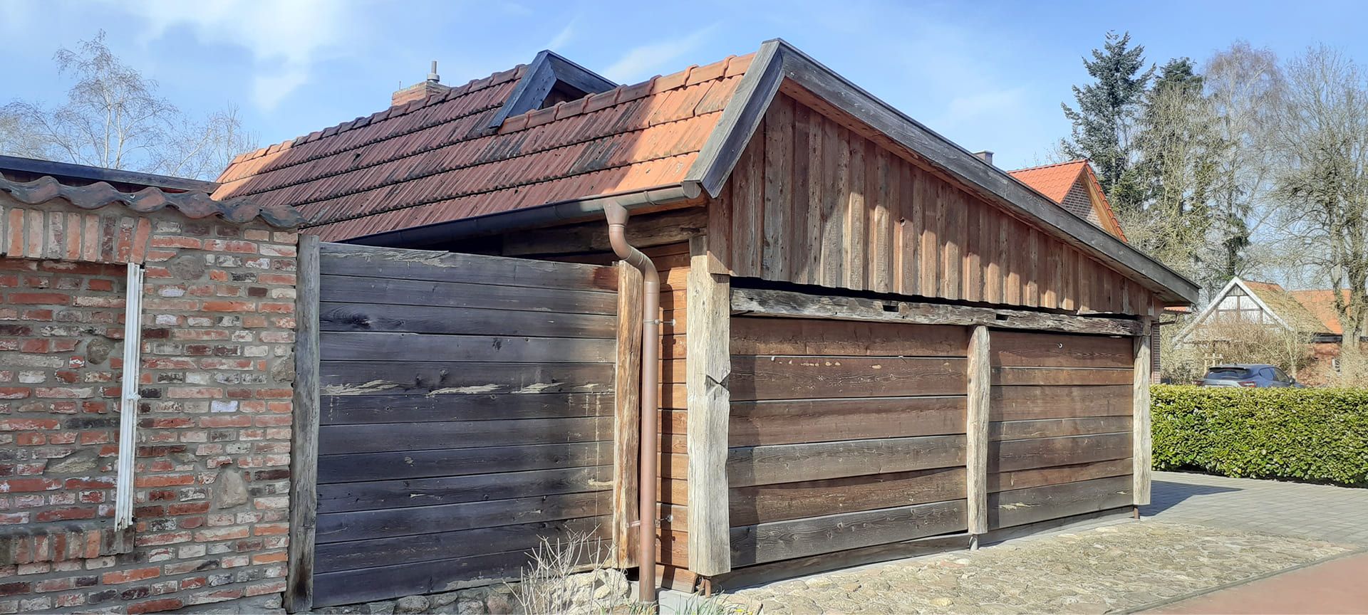 Holzgarage mit rotem Ziegeldach und angrenzender Holzwand